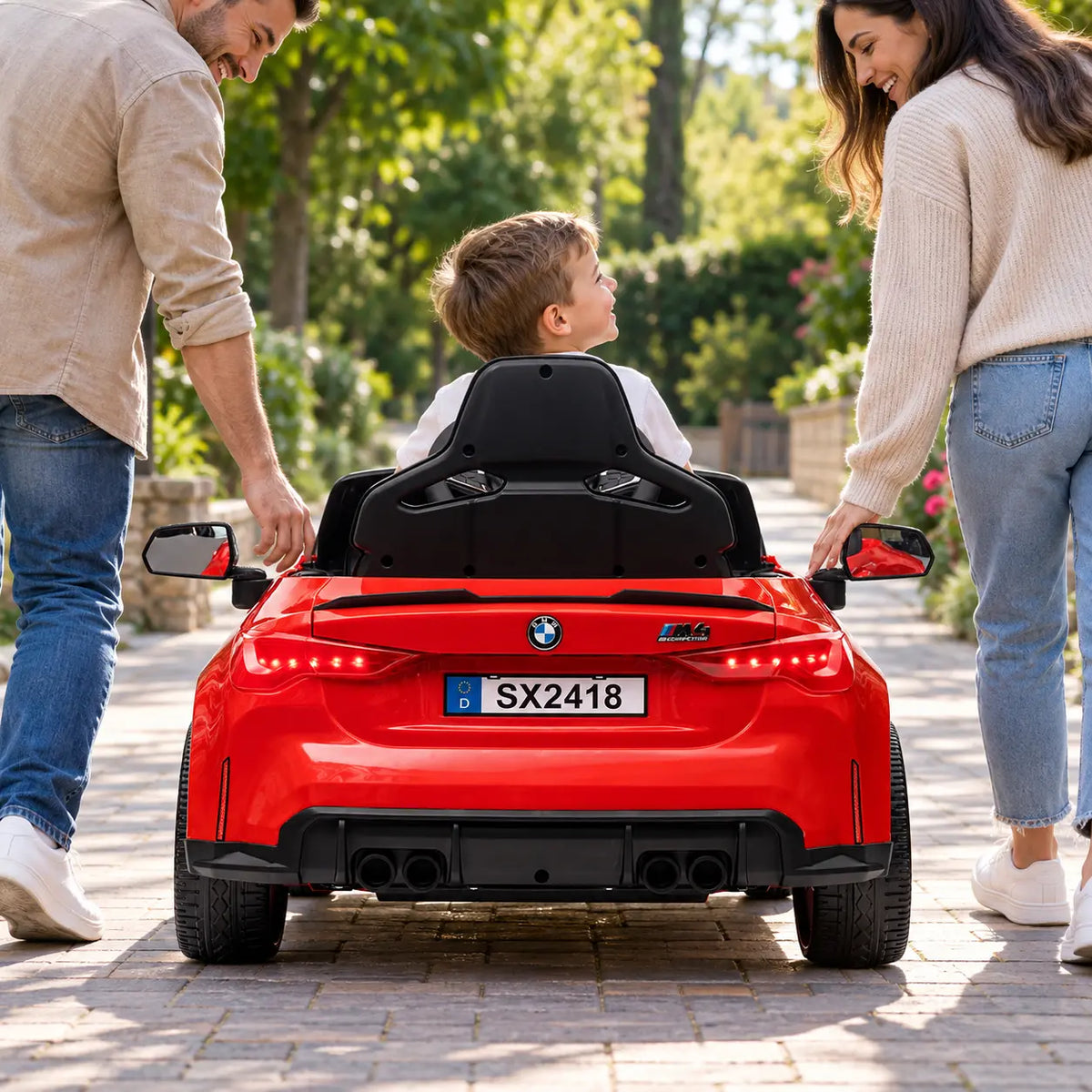 Mașinuță electrică KIDOO® BMW M4 roșie, cu un copil la volan și părinții alături, vedere din spate